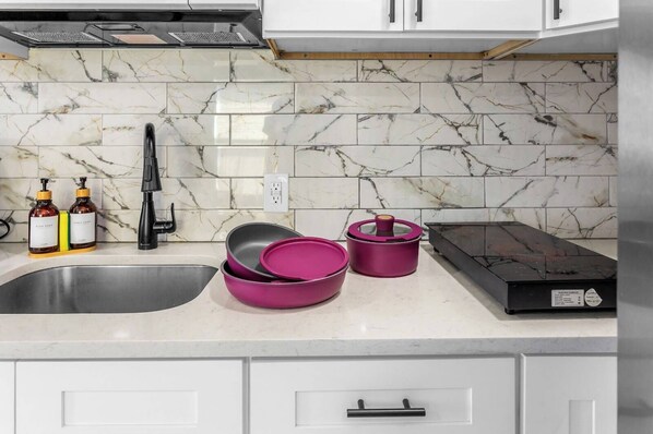 A kitchen with a marble backsplash, a stainless steel sink, and a black range hood.