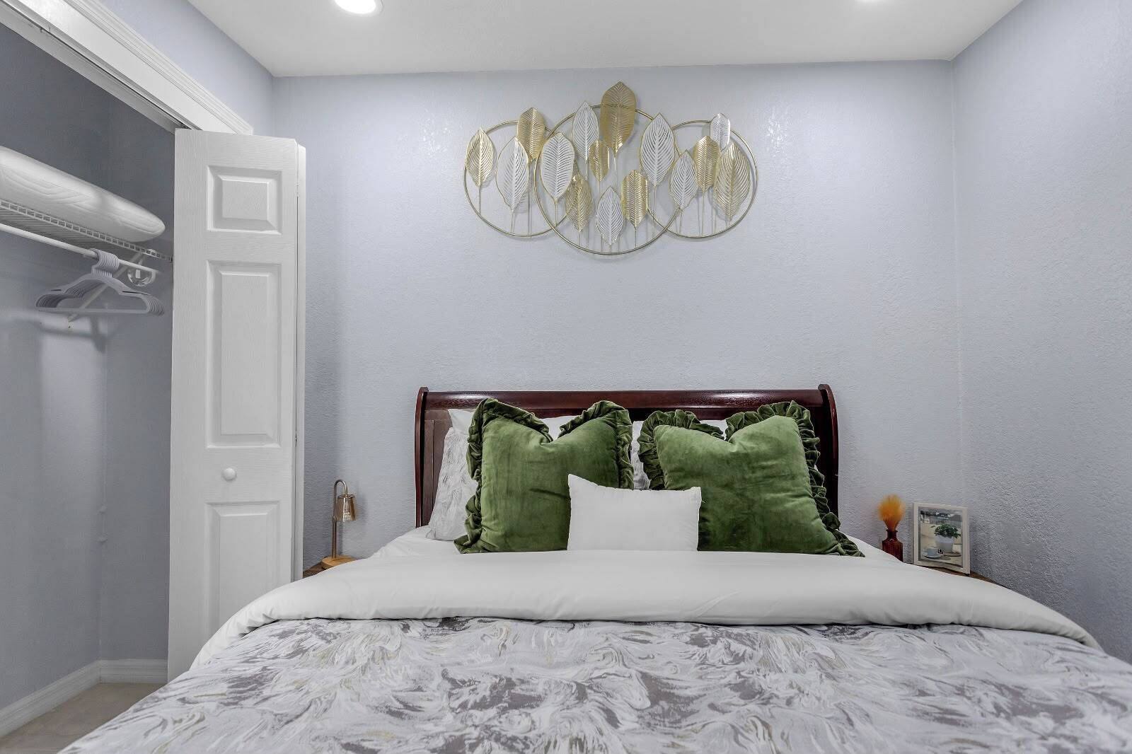 A bedroom with a bed, a wooden headboard, a wall-mounted decorative leaf art piece, and a white door.