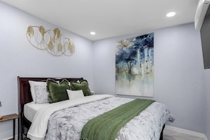 A bedroom with a bed, pillows, a green throw, a wall art piece, and a ceiling light.