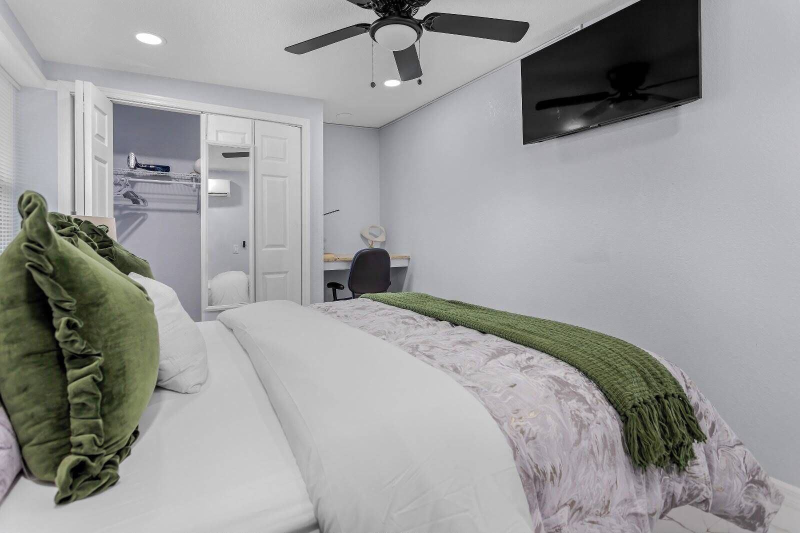 A bedroom with a bed, a desk, a chair, a ceiling fan, and a wardrobe.