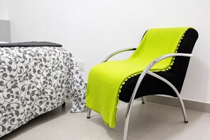 A room with a bed covered in a patterned bedspread, a bright green chair with a black cushion, and a white wall.