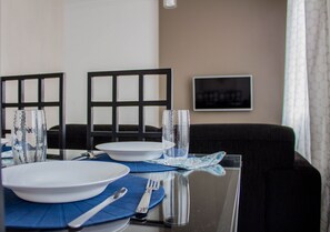A dining table set with plates, cutlery, and glasses, with a black chair and a framed picture on the wall.