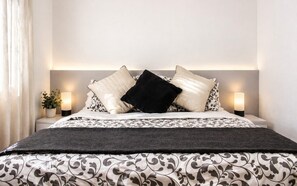A neatly made bed with a patterned bedspread, two bedside lamps, and a potted plant on the nightstand.