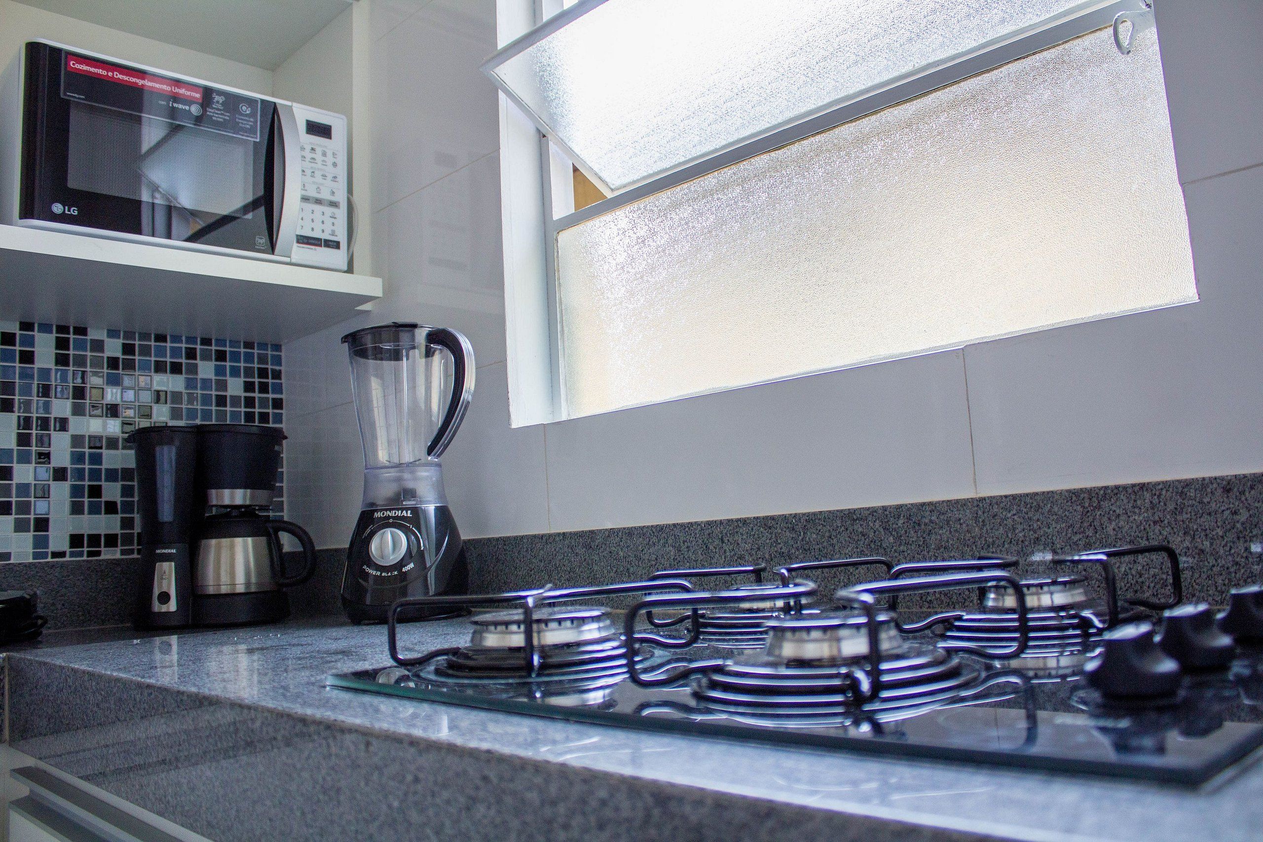 Uma cozinha com fogão a gás, cafeteira e micro-ondas.
