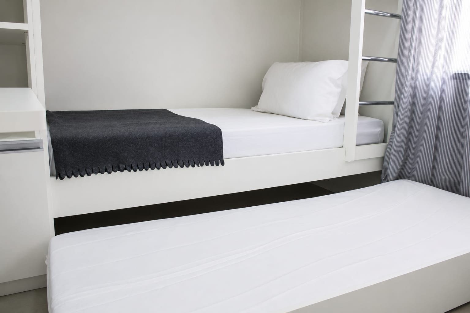 Una cama litera con un colchón blanco y negro, una almohada blanca y una manta gris.