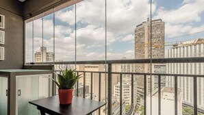 A balcony with a potted plant, a table, and a view of a cityscape with tall buildings. - Studio in Condo With Pool in Republica Thk1902 (São Paulo)