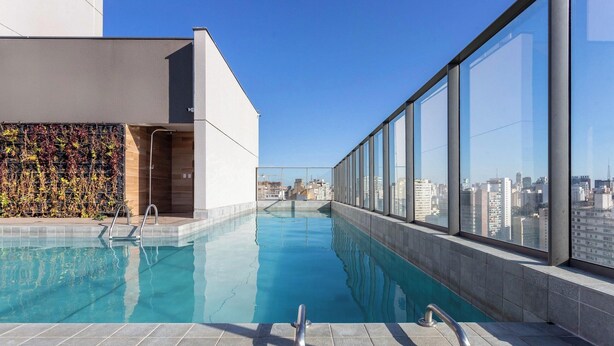 A rooftop pool with clear blue water, surrounded by large windows offering city views. - Studio in Condo With Pool in Republica Thk1902 (São Paulo)
