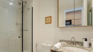A modern bathroom with a glass-enclosed shower, a toilet, a sink with a granite countertop, and a mirror reflecting a kitchen area. - Studio in Condo With Pool in Republica Thk1902 (São Paulo)