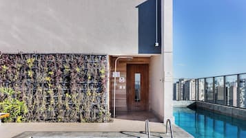 Ein modernes Gebäude mit Dachpool, vertikaler Begrünung und freiem Blick auf die Stadtlandschaft.