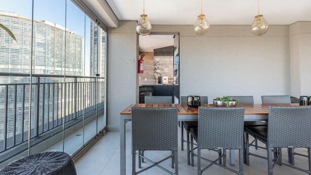 Ein moderner Essbereich mit Holztisch und Korbstühlen, großen Fenstern mit Blick auf die Stadt und hängenden Pendelleuchten.