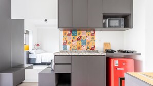 Eine kleine Küche mit grauen Schränken, einer Mikrowelle, einem roten Kühlschrank und einer farbenfrohen Spritzschutzwand.