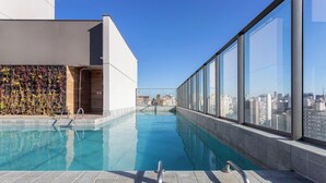 A rooftop pool with clear blue water, a modern building with a white facade, and a cityscape view through large windows. - Complete Studio 350m From the Metro Thk0502 (São Paulo)