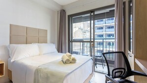 A hotel room with a bed, a chair, and a large window with a view of buildings.