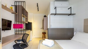 Habitació d'hotel senzilla amb llit, escriptori i cadira, televisió, petita cuina i bany.