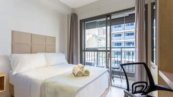 Een hotelkamer met een bed, een stoel en een groot raam met uitzicht op gebouwen.