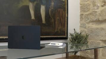 A laptop on a glass table with a framed painting in the background.