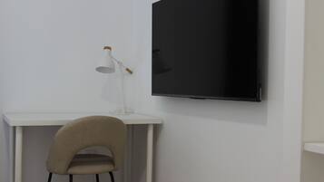 Et værelse med et hvidt skrivebord, en stol og et fladskærms-tv monteret på væggen.