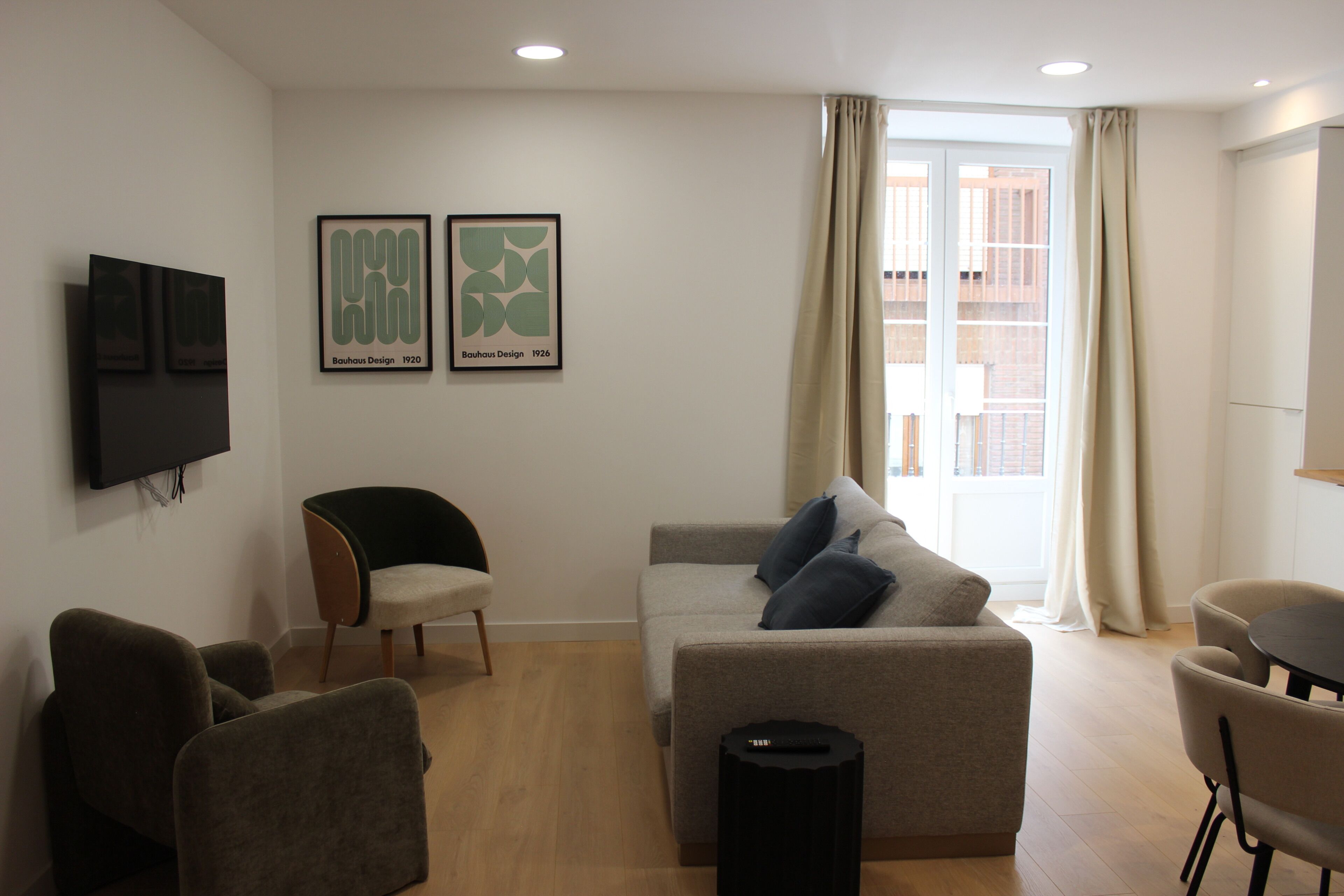 Ein Wohnzimmer mit einer Couch, Sesseln, einem Fernseher und gerahmten Kunstwerken an der Wand.