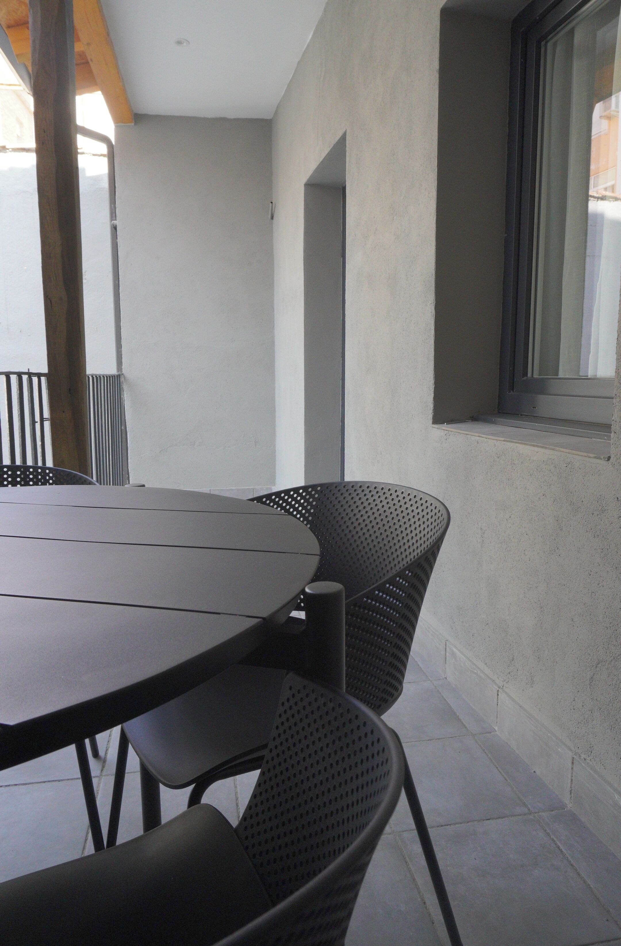 Un patio con una mesa redonda y dos sillas, una ventana con vistas y un muro de concreto.