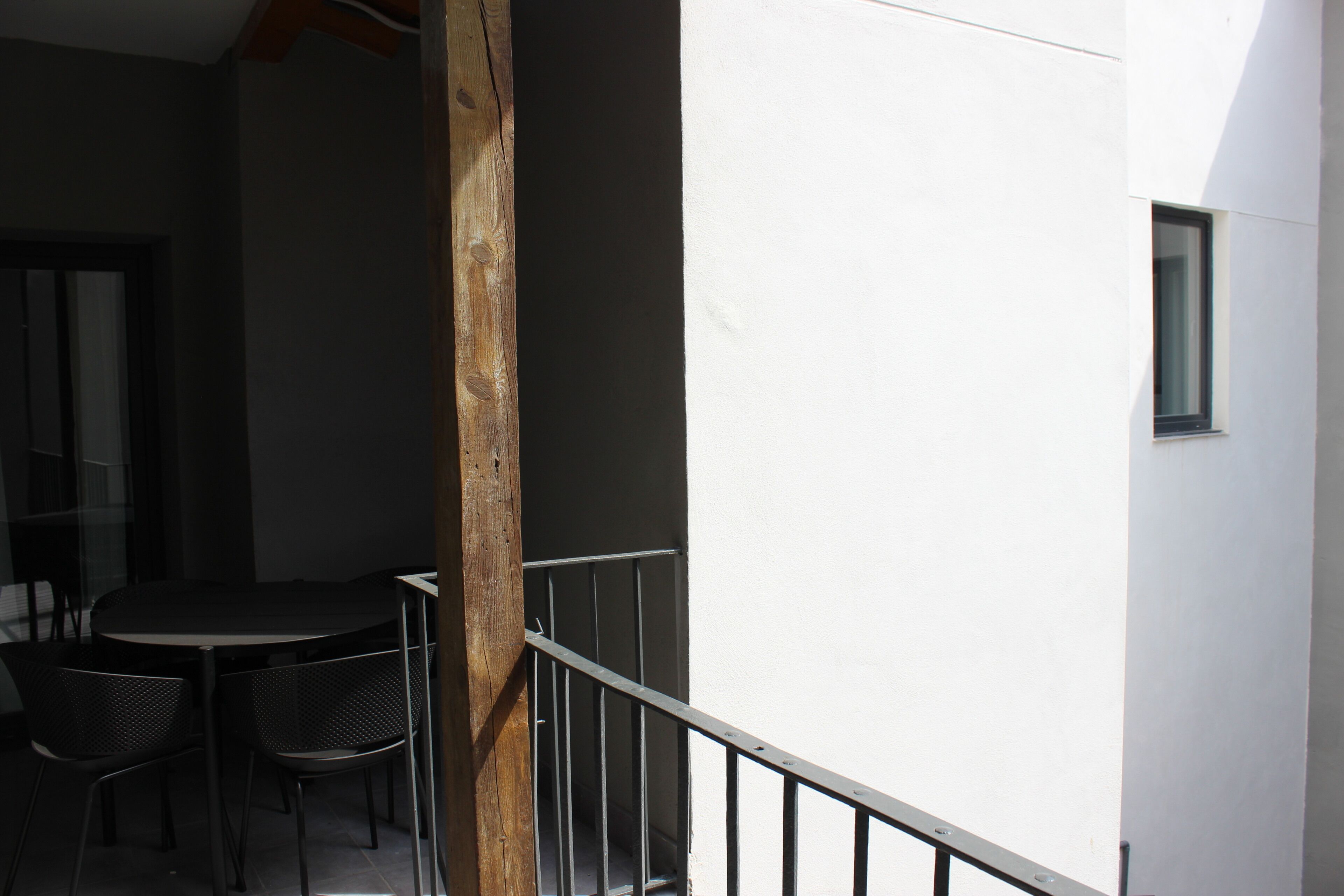 A balcony with a table and chairs, a wooden post, and a white wall.