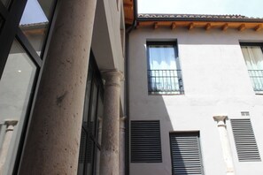 Un edificio con una columna, ventanas con contraventanas y un techo de madera.