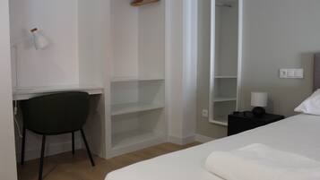 A bedroom with a bed, a desk with a chair, a wardrobe, and a bedside table with a lamp.