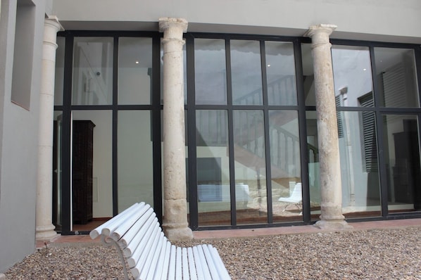 A building entrance with large glass doors, a white bench, and stone columns.