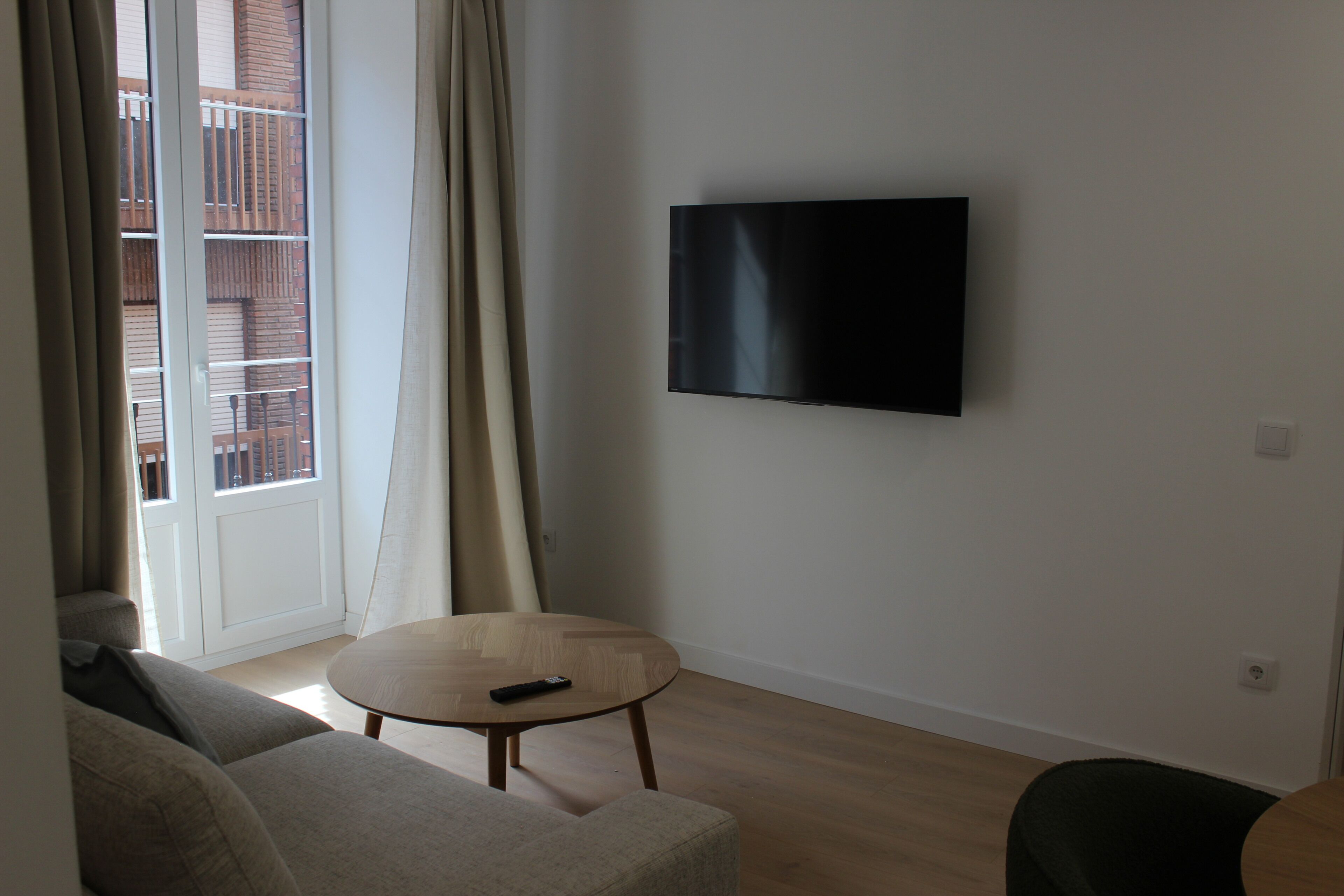 Una sala de estar con un televisor de pantalla plana montado en la pared, una mesa redonda de madera y un sofá.