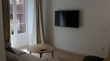 Una sala de estar con un televisor de pantalla plana montado en la pared, una mesa redonda de madera y un sofá.