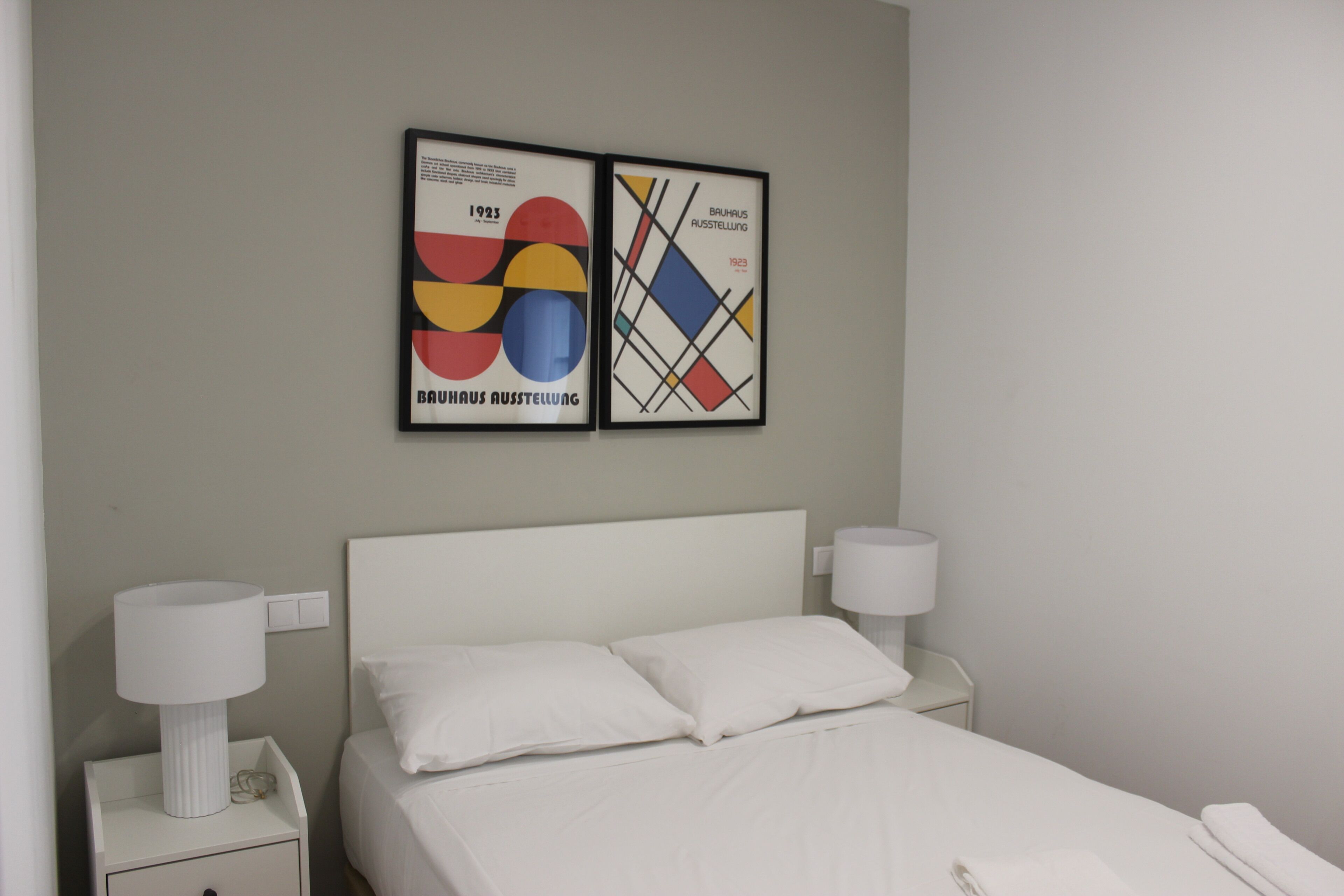 Een hotelkamer met een bed, twee bedlampjes en twee abstracte kunstwerken in lijsten aan de muur.