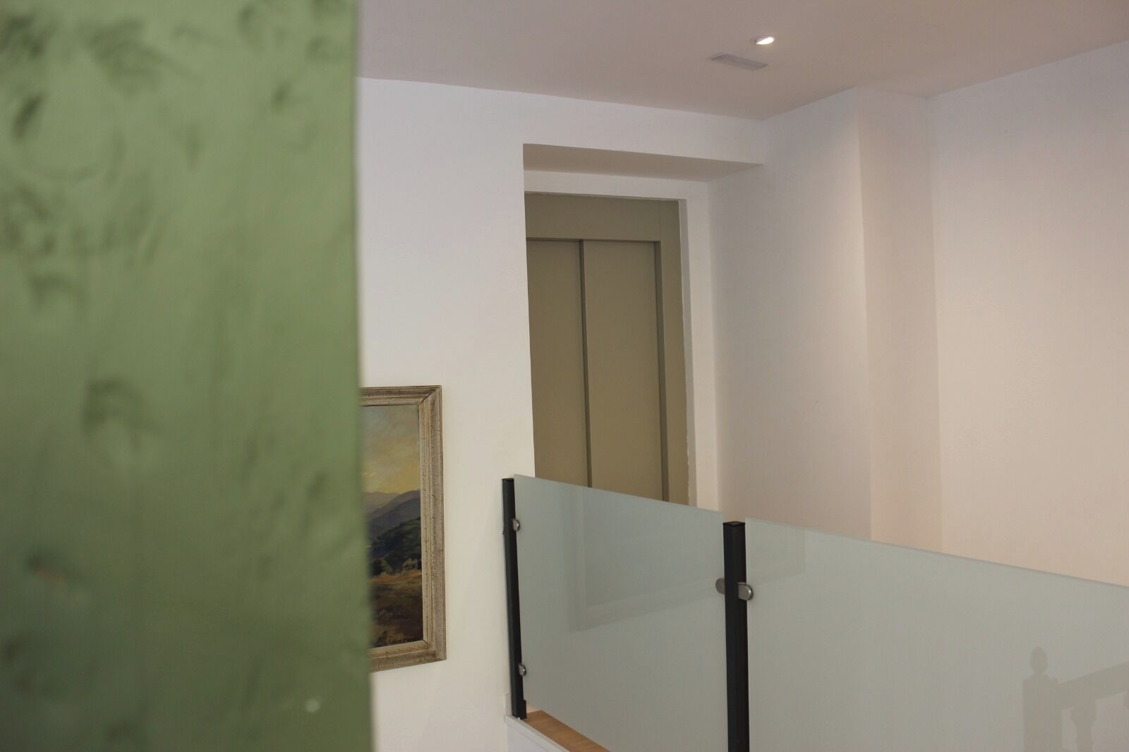 Una habitación con barandilla de vidrio, una puerta y un cuadro en la pared.