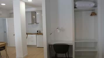 Een moderne, minimalistische kamer met een wit bureau, een stoel en een inbouwgarderobe met planken.