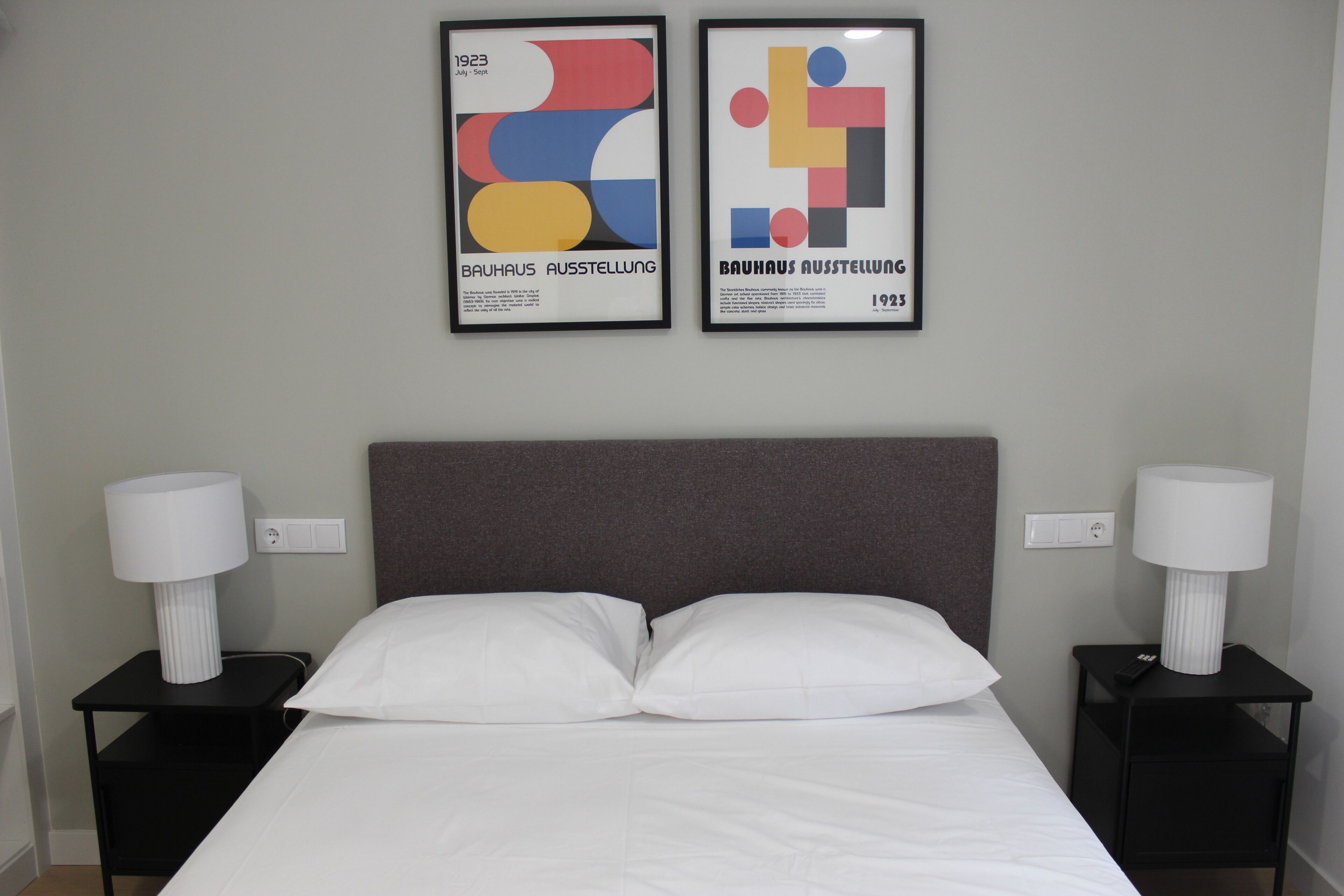 Quarto de hotel com uma cama, duas mesas de cabeceira, duas luminárias e duas obras de arte abstrata emolduradas na parede.