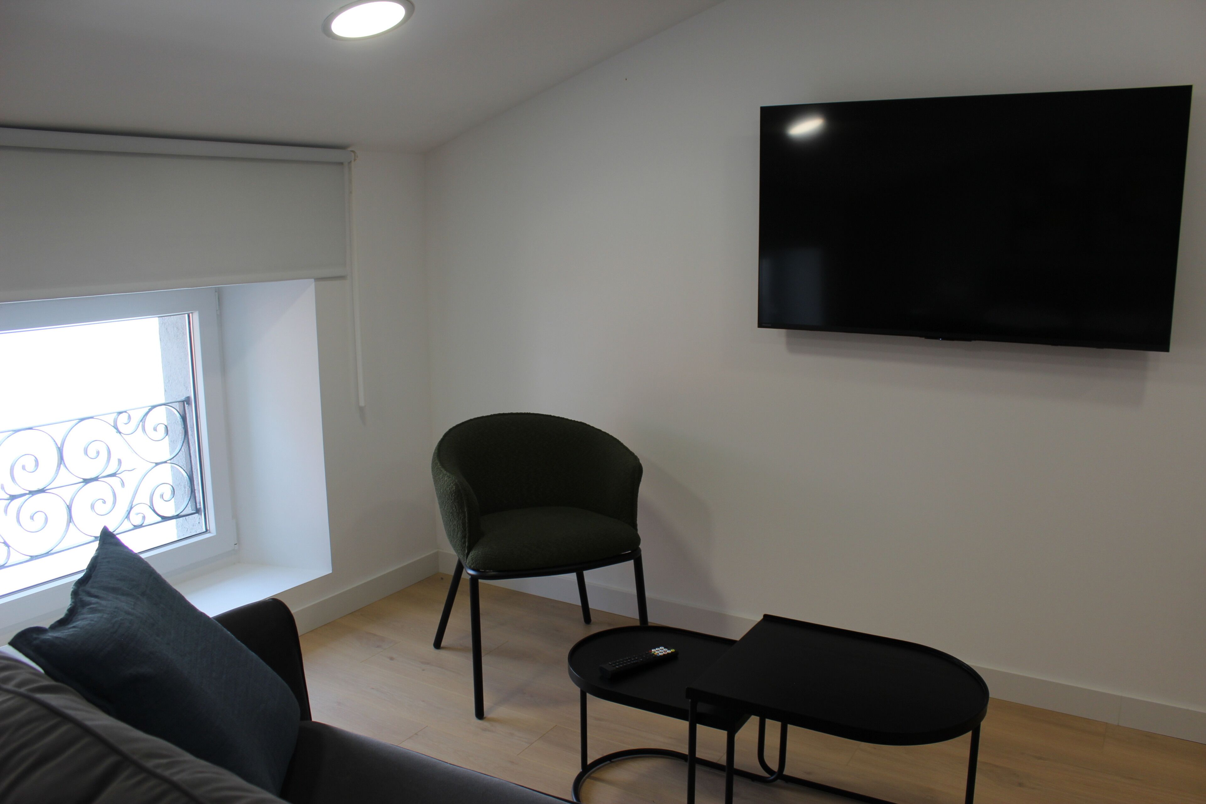 Un salon moderne avec un téléviseur à écran plat fixé au mur, un fauteuil vert foncé, une table basse noire et un canapé agrémenté d’un coussin noir.
