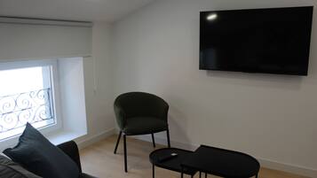 Un salon moderne avec un téléviseur à écran plat fixé au mur, un fauteuil vert foncé, une table basse noire et un canapé agrémenté d’un coussin noir.