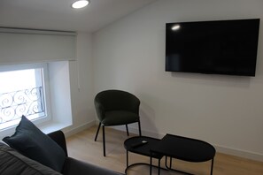 Una sala de estar moderna con un televisor de pantalla plana montado en la pared, un sillón verde oscuro, una mesa de centro negra y un sofá con un cojín negro.