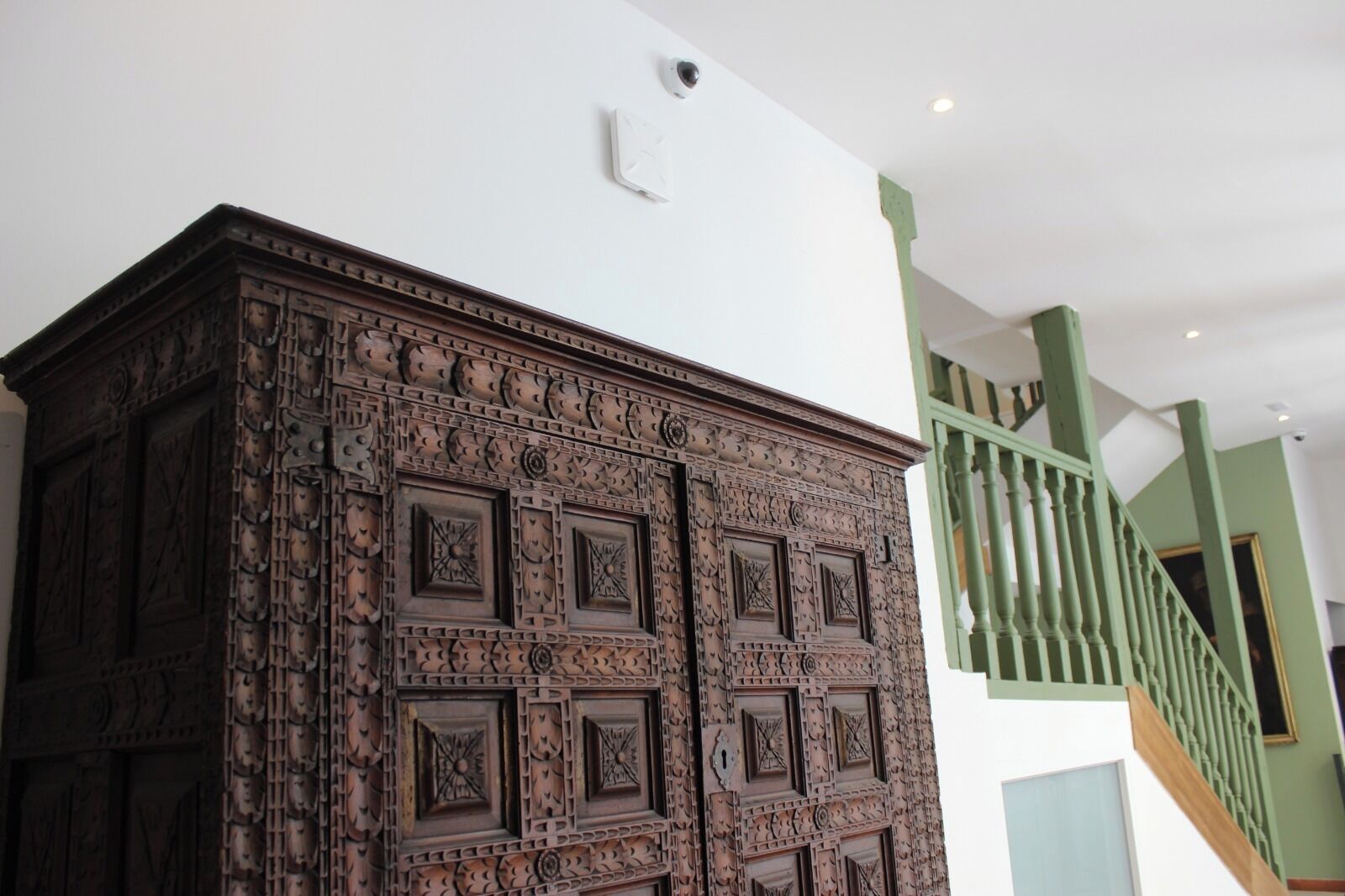 A wooden cabinet with intricate carvings, a green staircase railing, and a white ceiling with a light fixture.