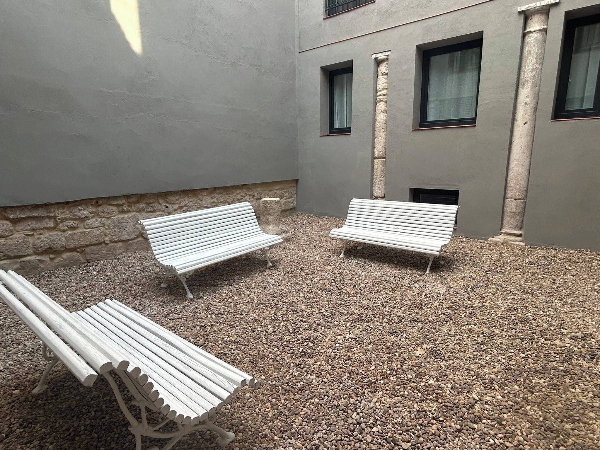 Un patio con dos bancos blancos y una pared de piedra.