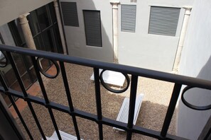 A balcony with a metal railing, a gravel ground, and a building with windows and vents. - Palacio Mambrilla (Valladolid)