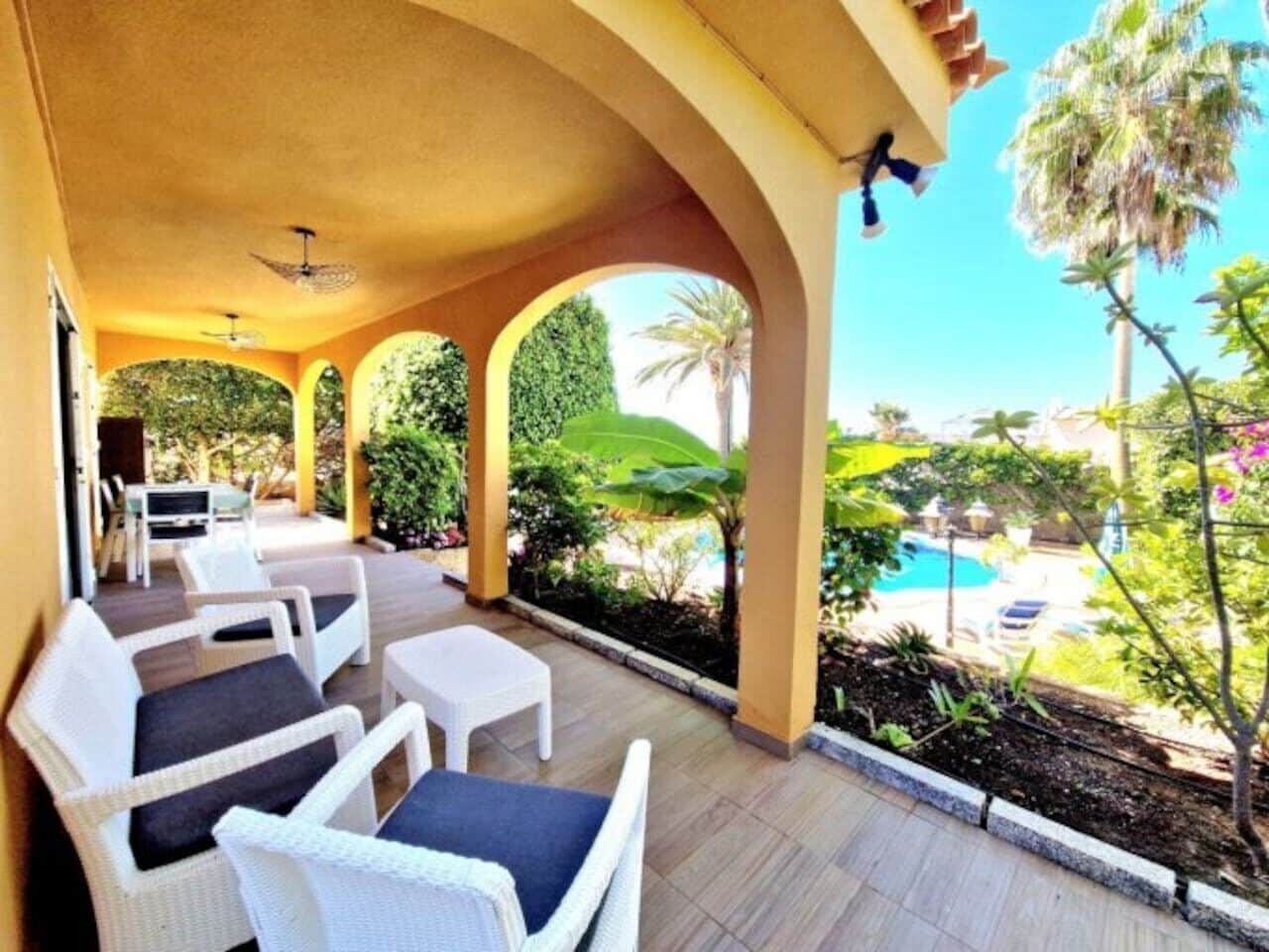 A covered outdoor seating area with wicker furniture and a view of a swimming pool.