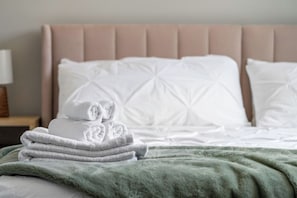 A neatly made bed with a green blanket and a stack of folded towels. - 3 King Beds | Min to UofC | Up and Down Unit (Calgary)