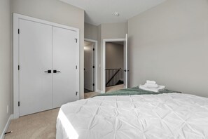 A bedroom with a bed, a closet, and a staircase leading to another room. - 3 King Beds | Min to UofC | Up and Down Unit (Calgary)