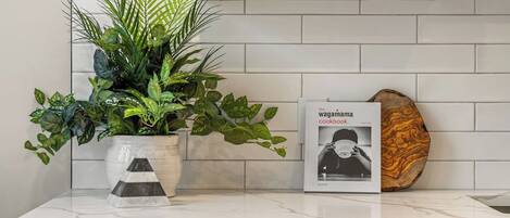 Un comptoir de cuisine agrémenté d’une plante en pot, d’un livre de recettes et d’un objet décoratif en bois.