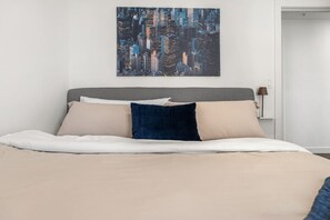 Uma cama com cabeceira cinza, roupa de cama bege e travesseiro azul escuro.