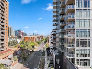 Um edifício residencial com vários andares, varandas, céu claro e uma rua arborizada.
