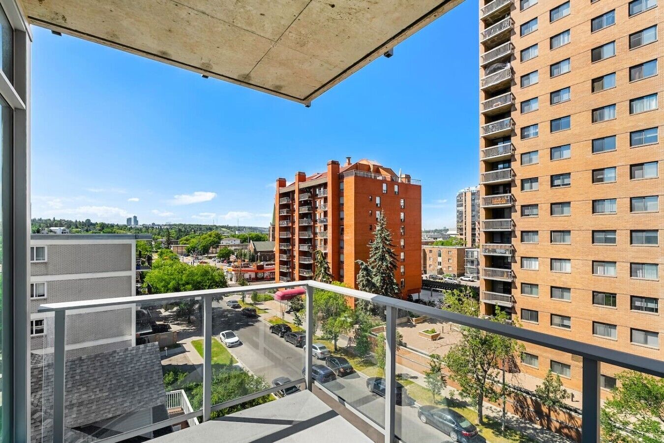 A balcony with a view of a parking area, a red brick building, and a high-rise apartment building.