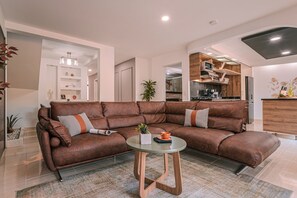 A modern living room with a brown leather sectional sofa, a glass coffee table, and a kitchen area with wooden cabinets and a microwave. - Private Jacuzzi, Rooftop & BBQ Loft in Medellín (Medellín)