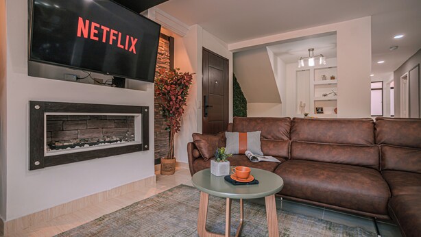 A living room with a brown leather sofa, a glass coffee table, a fireplace, and a flat-screen TV mounted above the fireplace. - Private Jacuzzi, Rooftop & BBQ Loft in Medellín (Medellín)