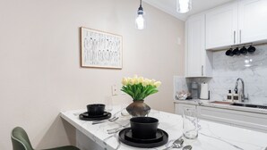 Ett modernt kök med vita skåp, en bänkskiva i marmor och en liten matplats med en grön stol.