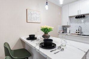 A modern kitchen with white cabinets, a marble countertop, and a small dining area with a green chair. - Fabulous 1-bedroom apartment with AC in vibrant Houston (Houston)